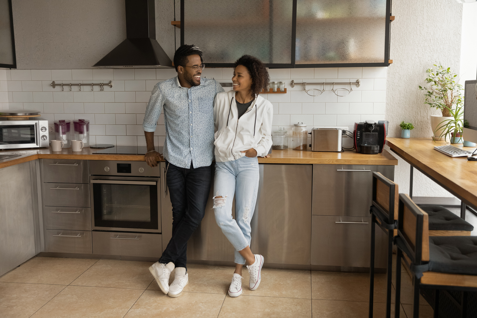 Happy affectionate young African American married family couple cuddling, enjoying communicating in modern stylish kitchen, talking speaking spending carefree weekend leisure time in own apartment.